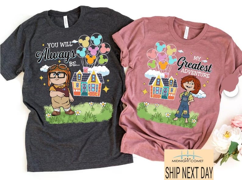 May include: Two t-shirts, one charcoal and one mauve, featuring cartoon graphics. The charcoal shirt says "You Will Always Be..." with a character, house, and balloons. The mauve shirt says "My Greatest Adventure" with a character, house, and balloons.