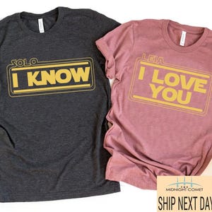 May include: Two t-shirts, one dark grey and one dusty rose, with a Star Wars theme. The grey shirt says "SOLO I KNOW" and the rose shirt says "LEIA I LOVE YOU". Both shirts have a yellow border around the text.