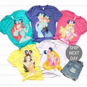 Pu&ograve; includere: Cinque magliette diverse con principesse Disney con orecchie da topo. Le magliette sono di vari colori, tra cui turchese, viola, rosa, giallo e bianco. Ogni maglietta presenta una principessa diversa, tra cui Ariel, Elsa e Anna, Aurora, Belle e Rapunzel.