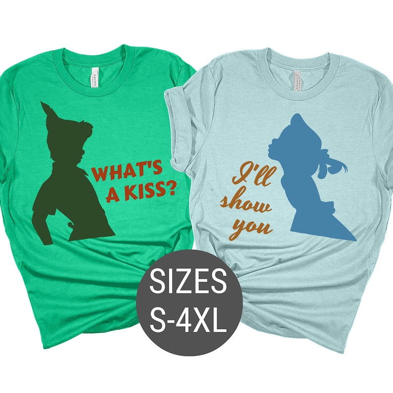 Peut inclure: Deux t-shirts, l'un vert et l'autre bleu, avec des silhouettes de Peter Pan et Wendy. Le t-shirt vert dit "What's a kiss?" et le t-shirt bleu dit "I'll show you".