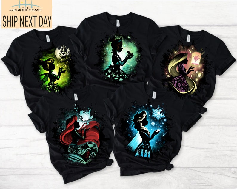 May include: Black t-shirts featuring colorful silhouette designs of popular fairytale characters. The shirts showcase characters like Tinkerbell, Ariel, and Rapunzel, with the text "MIDNIGHT COMET SHIP NEXT DAY" in the upper left corner.