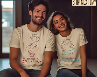 May include: A couple wearing matching t-shirts with a line drawing of Aladdin and Jasmine. The man's shirt says "I'm Her Street Rat" and the woman's shirt says "I'm His Princess".