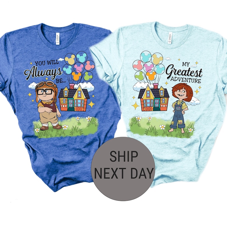 May include: Two t-shirts, one blue and one light blue, each with a colorful graphic. The blue shirt says "You Will Always Be..." with a cartoon character, house, and balloons. The light blue shirt says "My Greatest Adventure" with a cartoon character, house, and balloons.