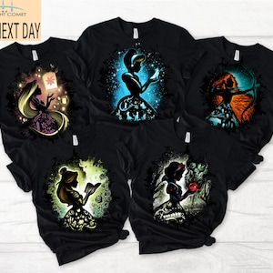 May include: Black t-shirts featuring colorful silhouette designs of fairytale characters. The designs include a princess with a lantern, a princess with a glowing ball, a princess with a bow and arrow, a princess reading a book, and a princess with an apple.