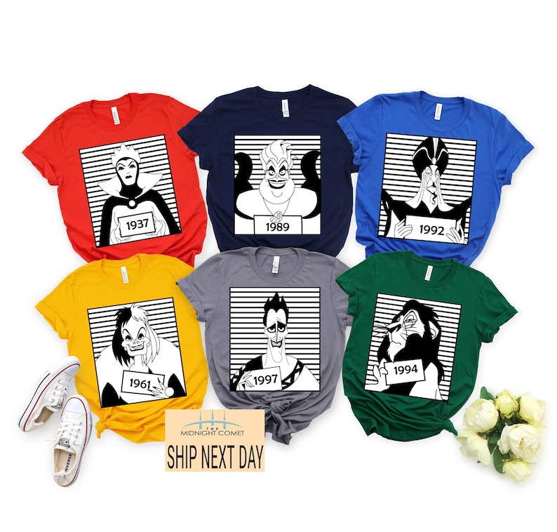 May include: A collection of colorful t-shirts featuring black and white illustrations of Disney villains. Each shirt displays a different character with a year on a prisoner-style placard. The shirts are red, navy, blue, yellow, gray, and green.