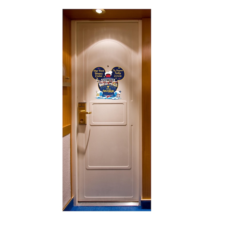 May include: A white door with a Mickey Mouse-shaped sign that reads "Our First Disney Cruise" and "The [Family Name] Family 2020." The sign features a cruise ship illustration and the word "Adventure" in blue.