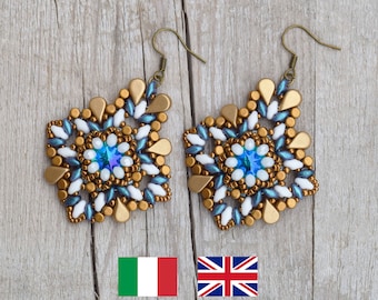 May include: A pair of gold, white, and blue beaded earrings with a teardrop shape. The earrings have a central blue crystal and are hanging from gold hooks.