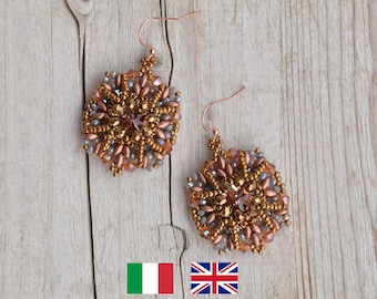 May include: A pair of gold and copper beaded earrings with a starburst design. The earrings are hanging from a wooden surface.