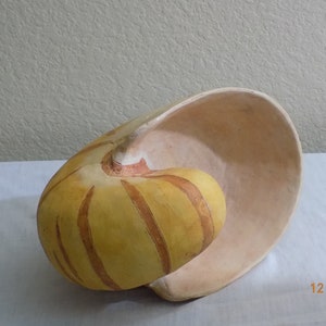 May include: A ceramic nautilus shell with a yellow and brown striped pattern. The shell is open and the inside is a light beige color.
