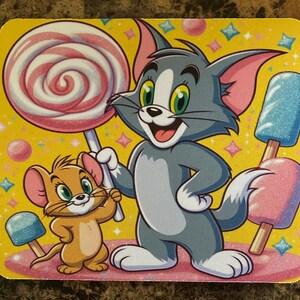 May include: A square, yellow mouse pad featuring Tom and Jerry cartoon characters. Tom, a gray cat, holds a large lollipop. Jerry, a brown mouse, stands beside Tom. The background is yellow with pink and blue popsicles.