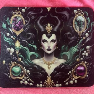 May include: A black and green mousepad with a detailed illustration of Maleficent from Disney's Sleeping Beauty. She is surrounded by swirling green and black patterns, pearls, and golden accents.