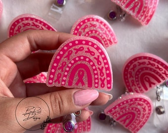 May include: Pink glitter rainbow badge reel with a pink ribbon design. The reel is made of resin and has a clear plastic badge holder.