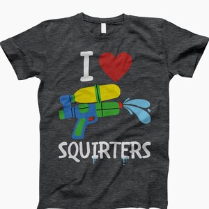 Op de afbeelding: Een donkergrijs T-shirt met de tekst "I love squirters" en een cartoon afbeelding van een waterpistool met een rood hart erboven.