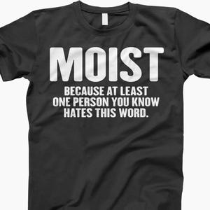 May include: Black t-shirt with the word "MOIST" in large white capital letters. Below, the text reads, "BECAUSE AT LEAST ONE PERSON YOU KNOW HATES THIS WORD."