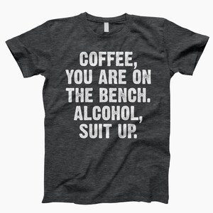 May include: Dark gray t-shirt with white text that reads "Coffee, you are on the bench. Alcohol, suit up."