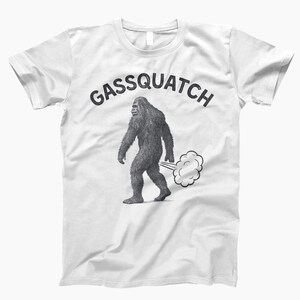 Puede incluir: Camiseta blanca con el texto "Gassquatch" sobre un dibujo en blanco y negro de una criatura parecida a Bigfoot caminando y emitiendo una nube de gas.