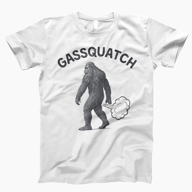 Puede incluir: Camiseta blanca con el texto "Gassquatch" sobre un dibujo en blanco y negro de una criatura parecida a Bigfoot caminando y emitiendo una nube de gas.