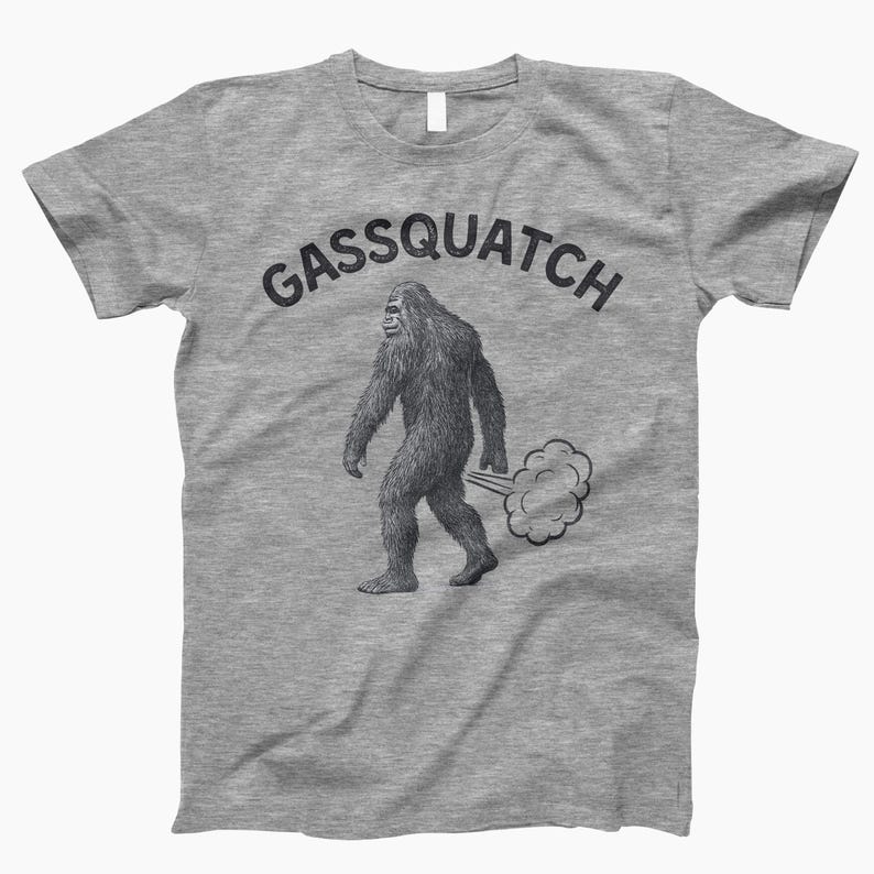 Puede incluir: Una camiseta gris jaspeado con un gr&aacute;fico de una criatura parecida a Pie Grande emitiendo una nube de gas. El texto "Gassquatch" est&aacute; arqueado sobre la ilustraci&oacute;n en negro. La camiseta tiene cuello redondo y mangas cortas.