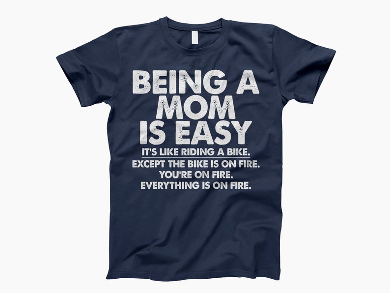 May include: Navy blue t-shirt with white text that reads "Being a Mom is Easy. It's like riding a bike. Except the bike is on fire. You're on fire. Everything is on fire."