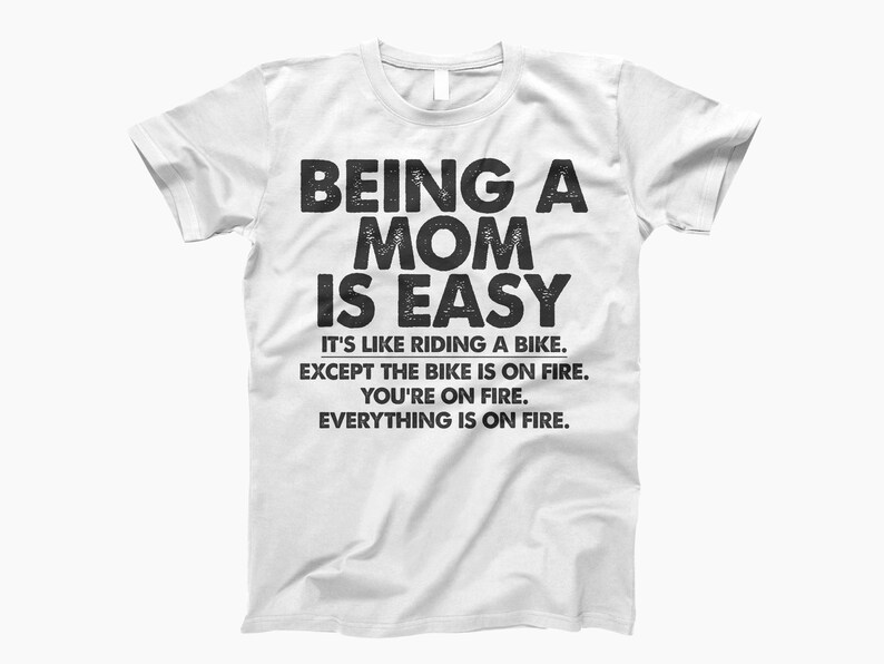 May include: White t-shirt with black text that reads "Being a Mom is Easy. It's like riding a bike, except the bike is on fire. You're on fire. Everything is on fire."
