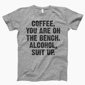 May include: Gray t-shirt with the text "Coffee, you are on the bench. Alcohol, suit up."