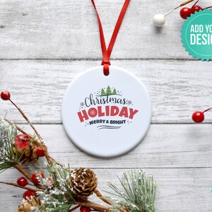 Pode incluir: Ornamento de cer&acirc;mica branca com uma fita vermelha pendurada em uma superf&iacute;cie de madeira branca. O ornamento tem um design verde e vermelho com o texto "Christmas Holiday Merry & Bright".