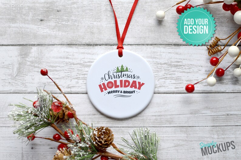 Pode incluir: Ornamento de cer&acirc;mica branca com uma fita vermelha pendurada em uma superf&iacute;cie de madeira branca. O ornamento tem um design verde e vermelho com o texto "Christmas Holiday Merry & Bright".