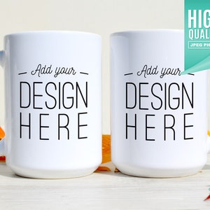 Pode incluir: Duas canecas de cerâmica branca com texto preto que diz "Add your - DESIGN HERE" sobre uma superfície de madeira branca com folhas de outono.