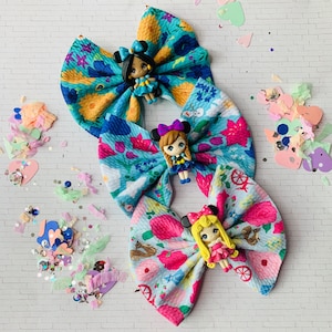 May include: Three fabric hair bows with a princess character on each. The bows are in shades of blue, green, and pink with floral patterns.