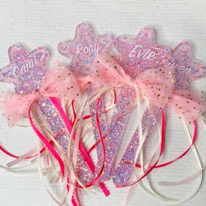 May include: Three pink star-shaped wands with glitter and pink tulle bows. The wands are decorated with the names "RORY", "EVIE", and "CAMI" in white lettering.