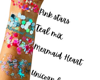 May include: A close-up of a person's arm with five different types of glitter applied in rows. The glitter is labeled "Unicorn Love", "Mermaid Heart", "Teal Mix", "Mermaid Tails", and "Pink Stars".