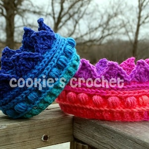 May include: Two crocheted crowns, one in shades of blue and green, the other in pink, purple, and red. The crowns are made with a textured stitch and have a scalloped edge.