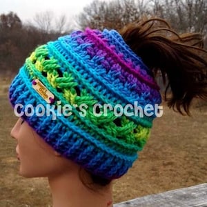May include: A colorful crocheted hat with a ponytail hole. The hat is made in a rainbow of colors, including blue, green, purple, and yellow. The hat has a small wooden tag that says "Cookie's Crochet".