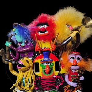 May include: A colorful, whimsical sculpture of a band, featuring various Muppet-like characters playing instruments. The band includes a drummer, trumpet player, guitarist, and vocalist, all with unique features and vibrant colors. The band is set against a black background.