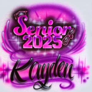 Puede incluir: Camiseta blanca con un diseño aerografiado que presenta una gorra de graduación rosa y morada, el texto "Senior 2025" y el nombre "Kayden".