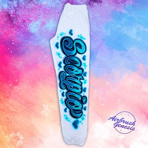 May include: White sweatpants with a blue and black airbrushed design of the word "Scorpio" on the left leg. The design includes hearts and stars.
