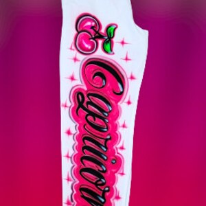 Puede incluir: Pantalones de ch&aacute;ndal blancos con una cereza rosa y la palabra "Capricornio" escrita en letras negras y rosas.