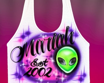 May include: White tank top with a purple and pink design featuring the name "Mariah" in black cursive lettering, the text "Est 2002" and a green alien head.
