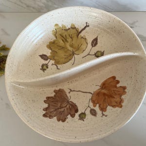 May include: Cream-colored, divided serving dish with a speckled finish. The dish features a curved divider and is decorated with brown and yellow leaf designs. A vintage-style serving piece.