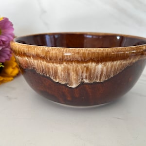 May include: A brown and white glazed ceramic bowl with a drip glaze design. The bowl is round and has a wide rim.