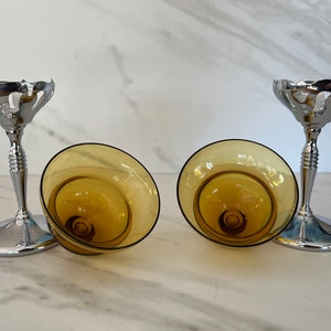 May include: Two champagne glasses with amber-colored bowls and silver-colored stems. The bowls are tilted, revealing their interior design. The stems have a decorative, ribbed design, and the bases are round.