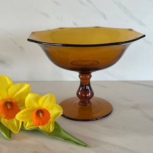 May include: A brown glass pedestal bowl with a scalloped rim. The bowl is on a white marble surface.