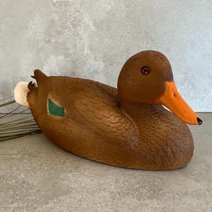Peut inclure: Un leurre de canard brun avec un détail d'aile verte et un bec orange. Le leurre est fait d'un matériau texturé qui ressemble à des plumes.