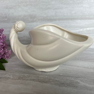 May include: A white ceramic planter shaped like a cornucopia with a curled handle. The planter has a smooth, glossy finish and is marked "USA 477".