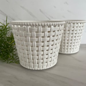 May include: Two white woven plastic baskets with a square pattern. The baskets are empty and sitting on a white marble surface.
