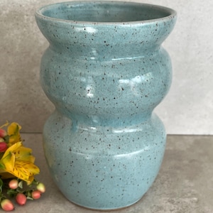May include: A turquoise ceramic vase with a speckled finish. The vase has a unique shape, with three stacked, rounded sections. The interior is smooth, and the exterior has a textured appearance. The vase is a decorative item.
