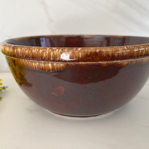 May include: A brown ceramic mixing bowl with a white glaze around the rim. The bowl is glazed in a brown and white pattern.