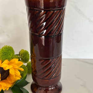 May include: A brown ceramic vase with a textured, woven design. The vase has a wide base and a narrow opening.