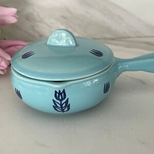 May include: A light blue ceramic casserole dish with a lid and a handle. The dish has a blue floral design.