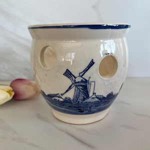 May include: White ceramic planter with a blue and white windmill design. The planter has three holes on the side.